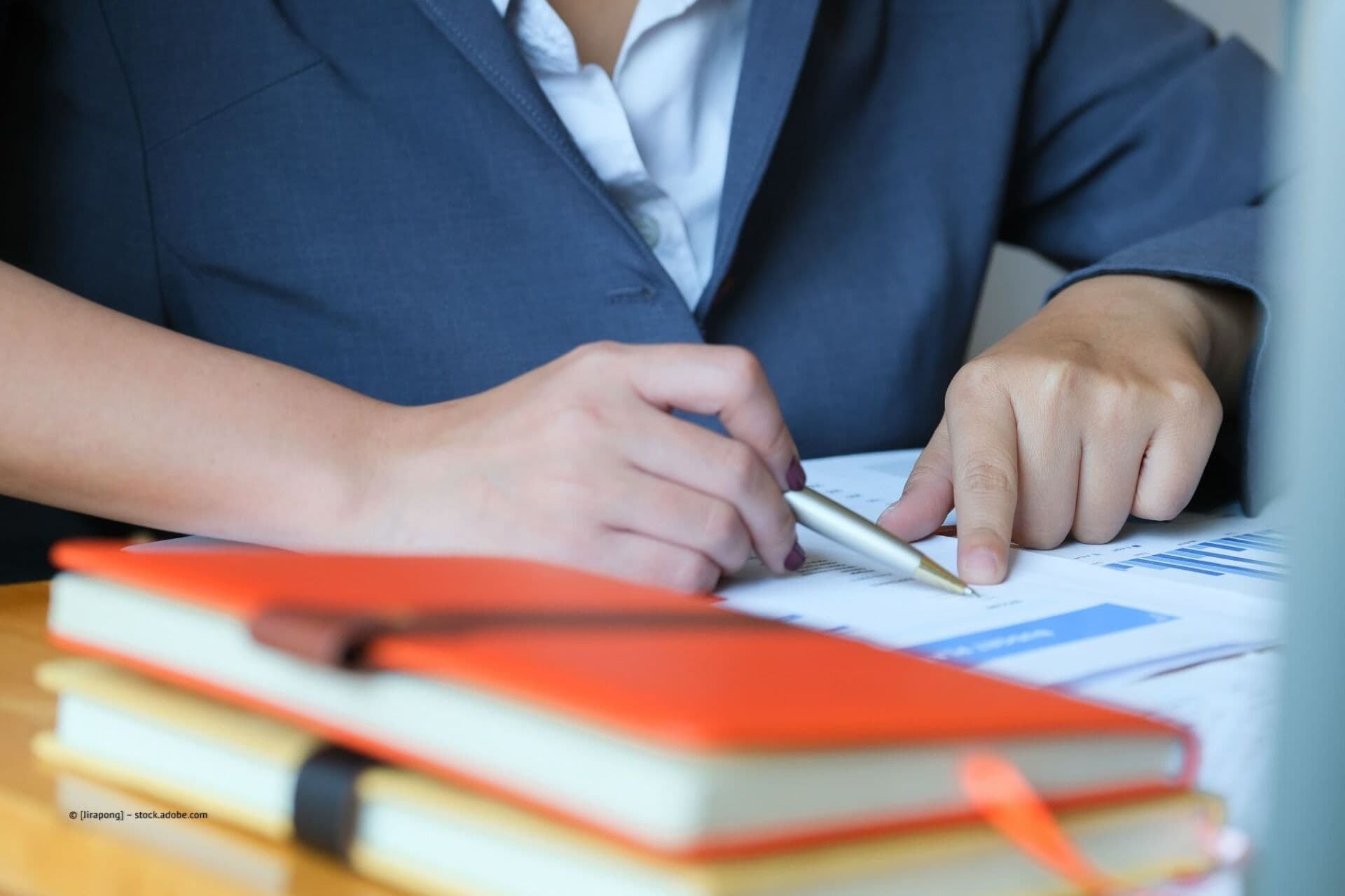 Beratung am Schreibtisch mit Unterlagen und orangem Notizbuch